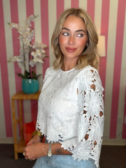 Woman wearing a white lace top in a room with striped walls.