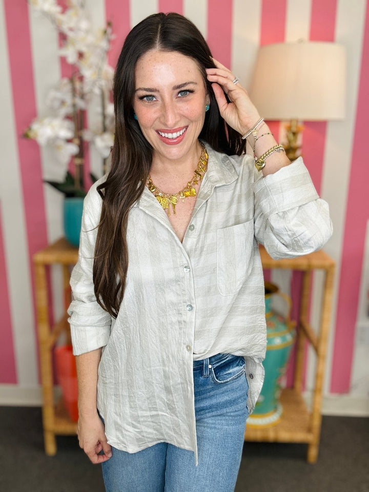 Woman wearing a light-colored shirt and blue jeans in front of a striped wall.