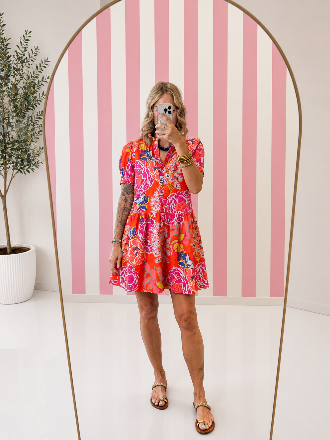 Woman wearing a colorful floral dress standing in front of a pink and white striped wall.