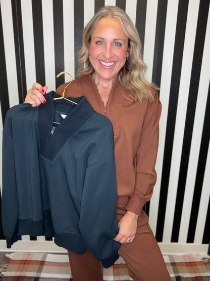 woman in a brown set holding a blue set standing in front of a striped wall