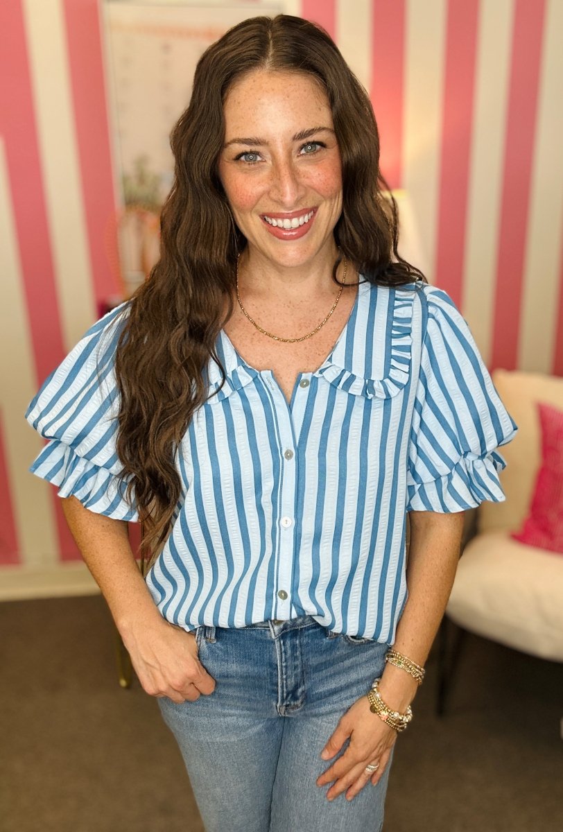 Woman wearing a blue and white striped shirt with ruffled sleeves in an indoor setting.