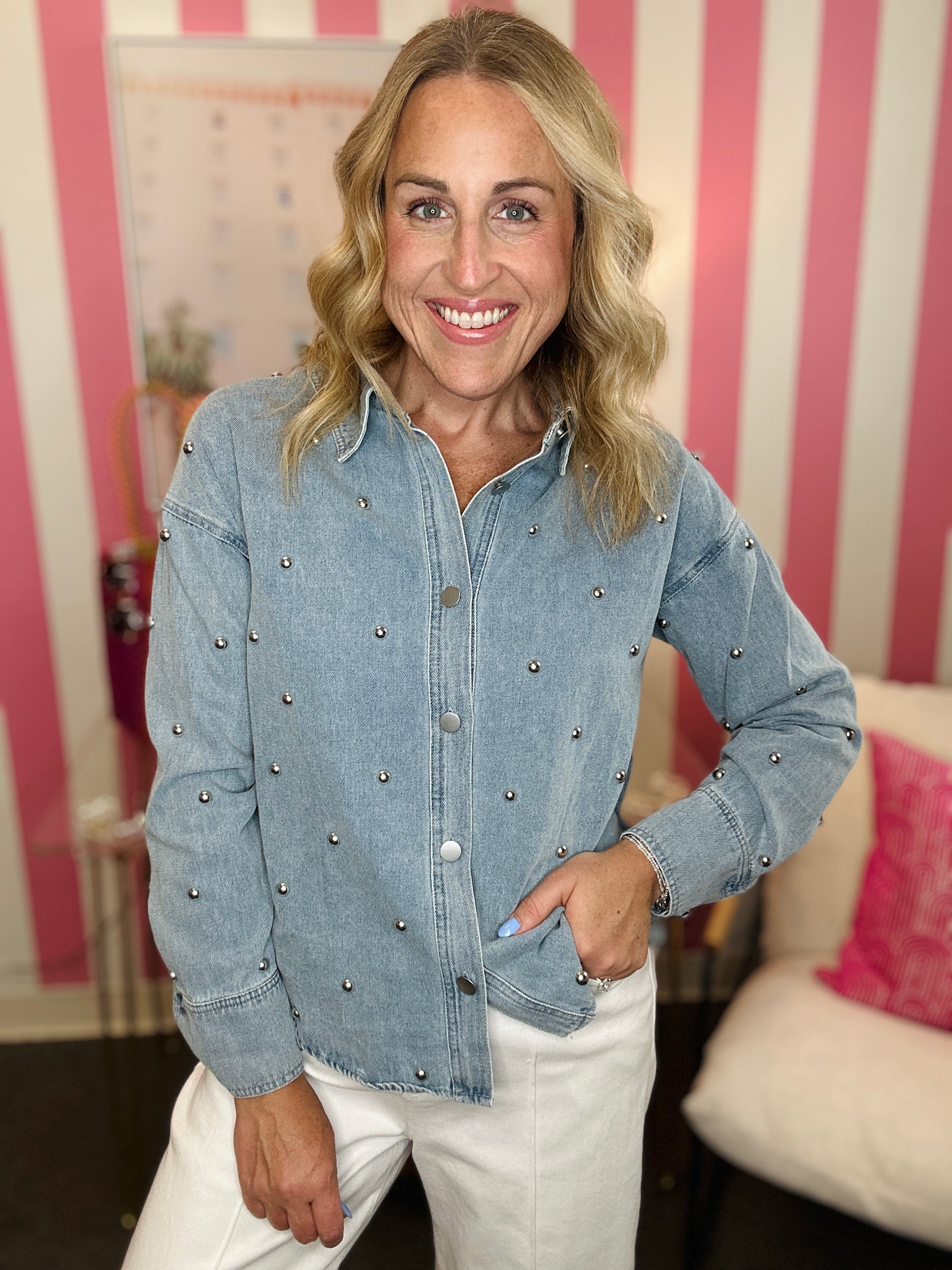Woman wearing a blue denim jacket with embellishments in a room with pink and white striped wallpaper.