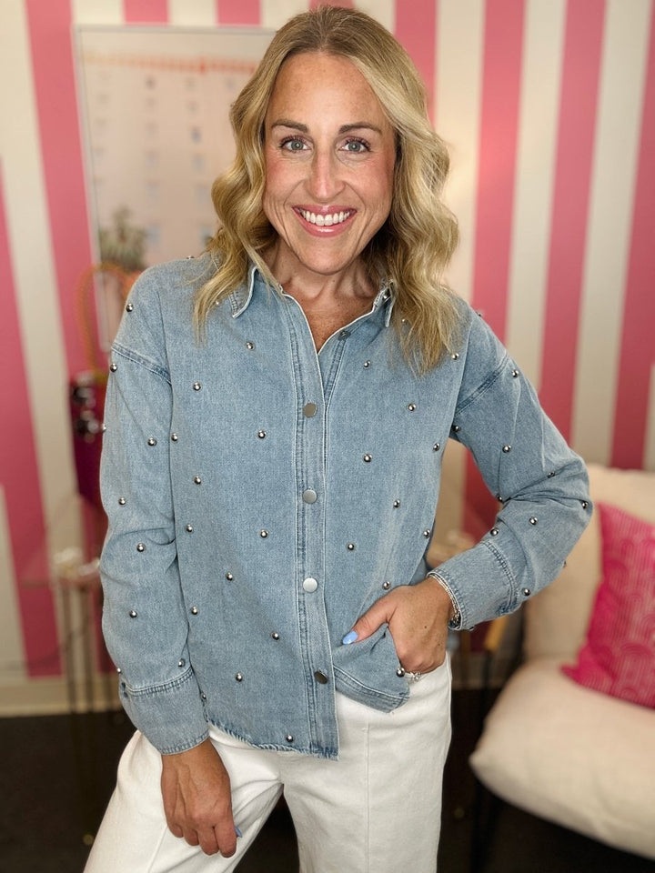 Woman wearing a blue denim jacket with embellishments in a room with pink and white striped wallpaper.