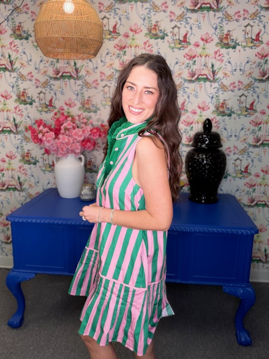 Woman in a green and pink striped dress standing in a room with floral wallpaper and a blue table.