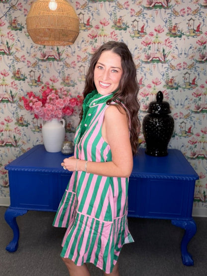 Woman in a green and pink striped dress standing in a room with floral wallpaper and a blue table.