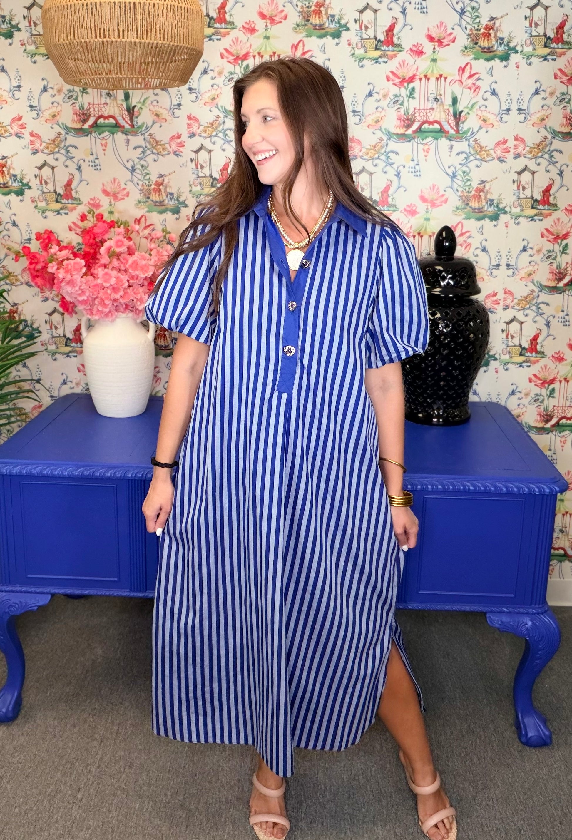Woman wearing a blue and white striped dress standing in front of a floral wallpapered wall.