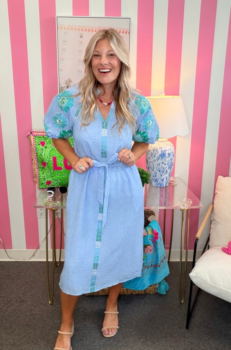 Woman in a light blue dress standing in a room with pink and white striped walls.
