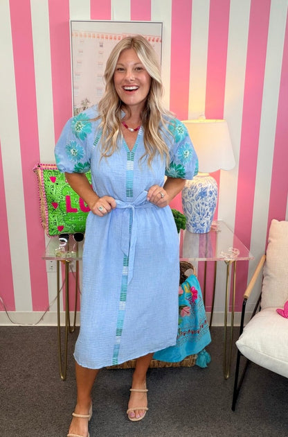 Woman in a light blue dress standing in a room with pink and white striped walls.