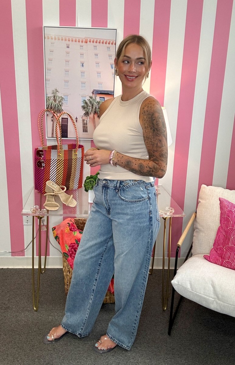 Woman in a white tank top and blue jeans standing in a room with pink and white striped walls.