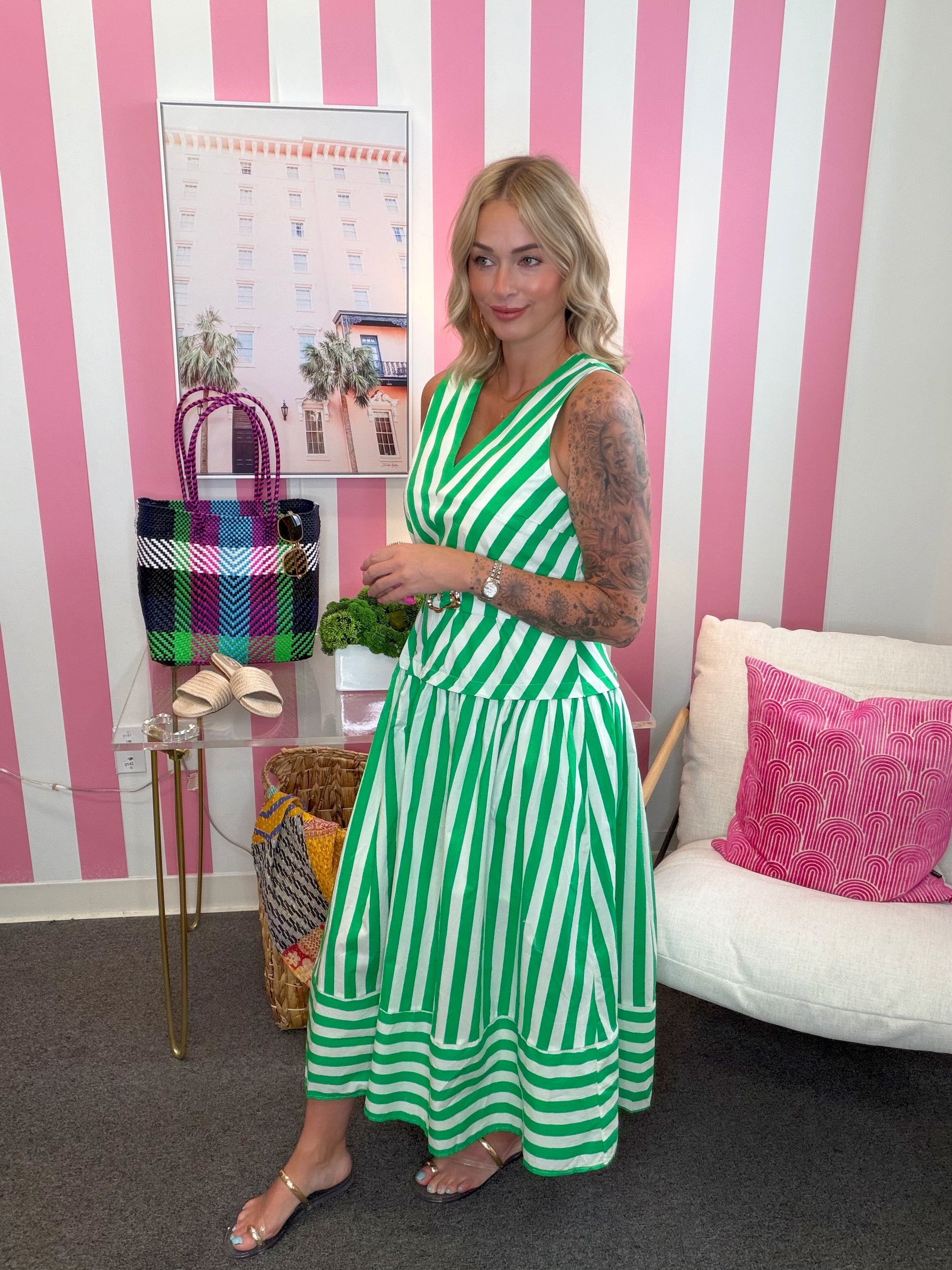 Woman in a green and white striped dress standing in a room with pink and white striped walls.
