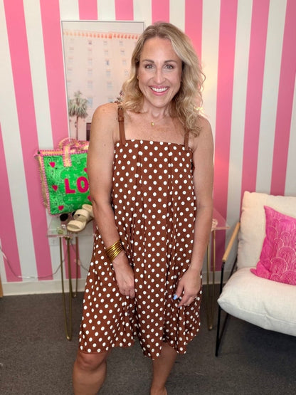 Woman in a brown polka dot dress standing in front of a pink and white striped wall.