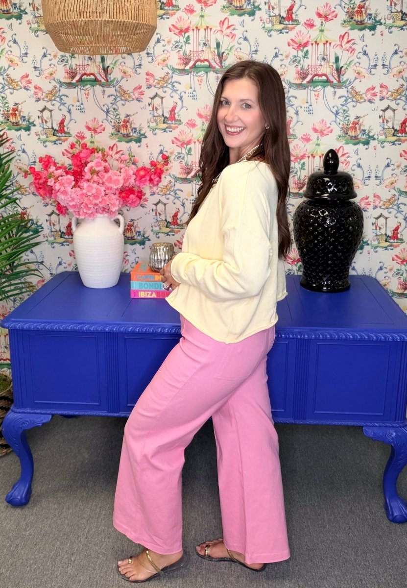 Woman in a yellow top and pink pants standing in front of a colorful floral-patterned wall.