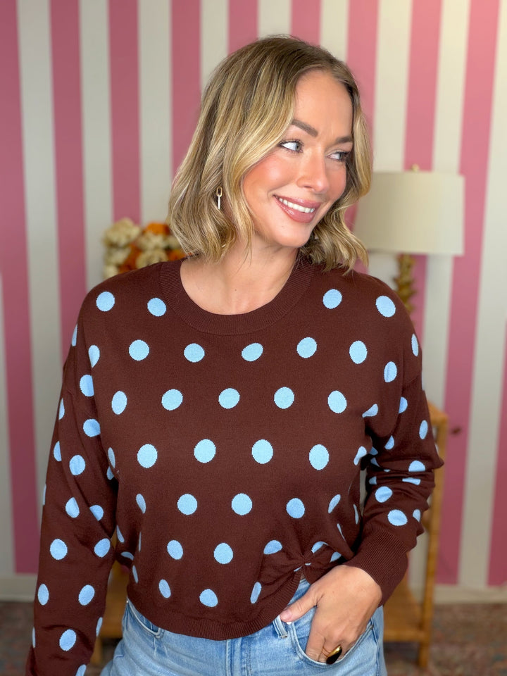 woman standing in brown sweater with blue polka dots