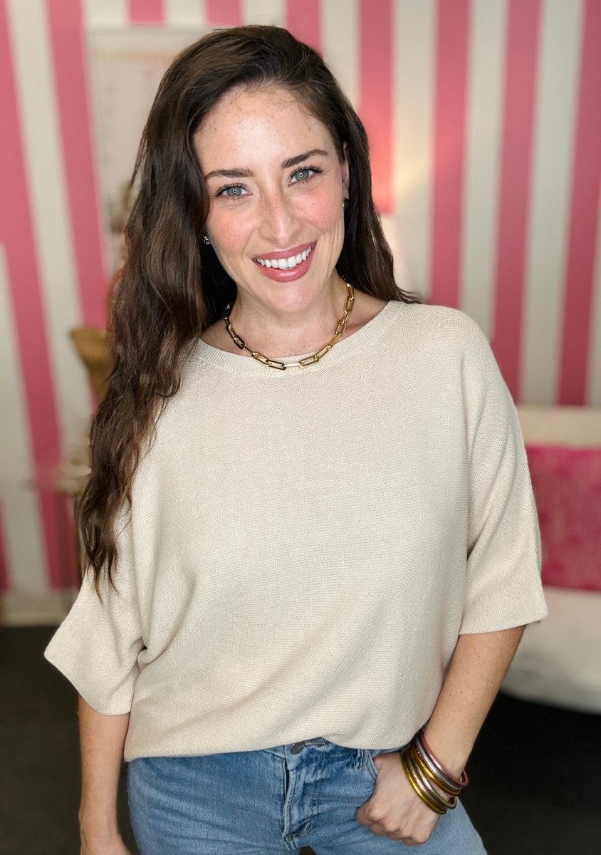 Woman wearing a beige sweater and blue jeans with a striped pink and white background