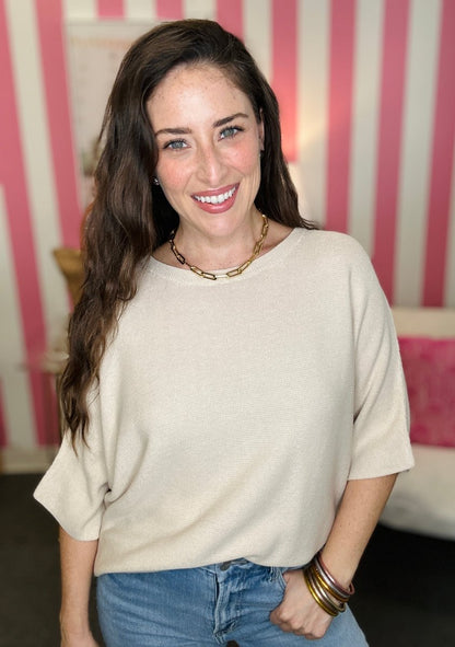 Woman wearing a beige sweater and blue jeans with a striped pink and white background