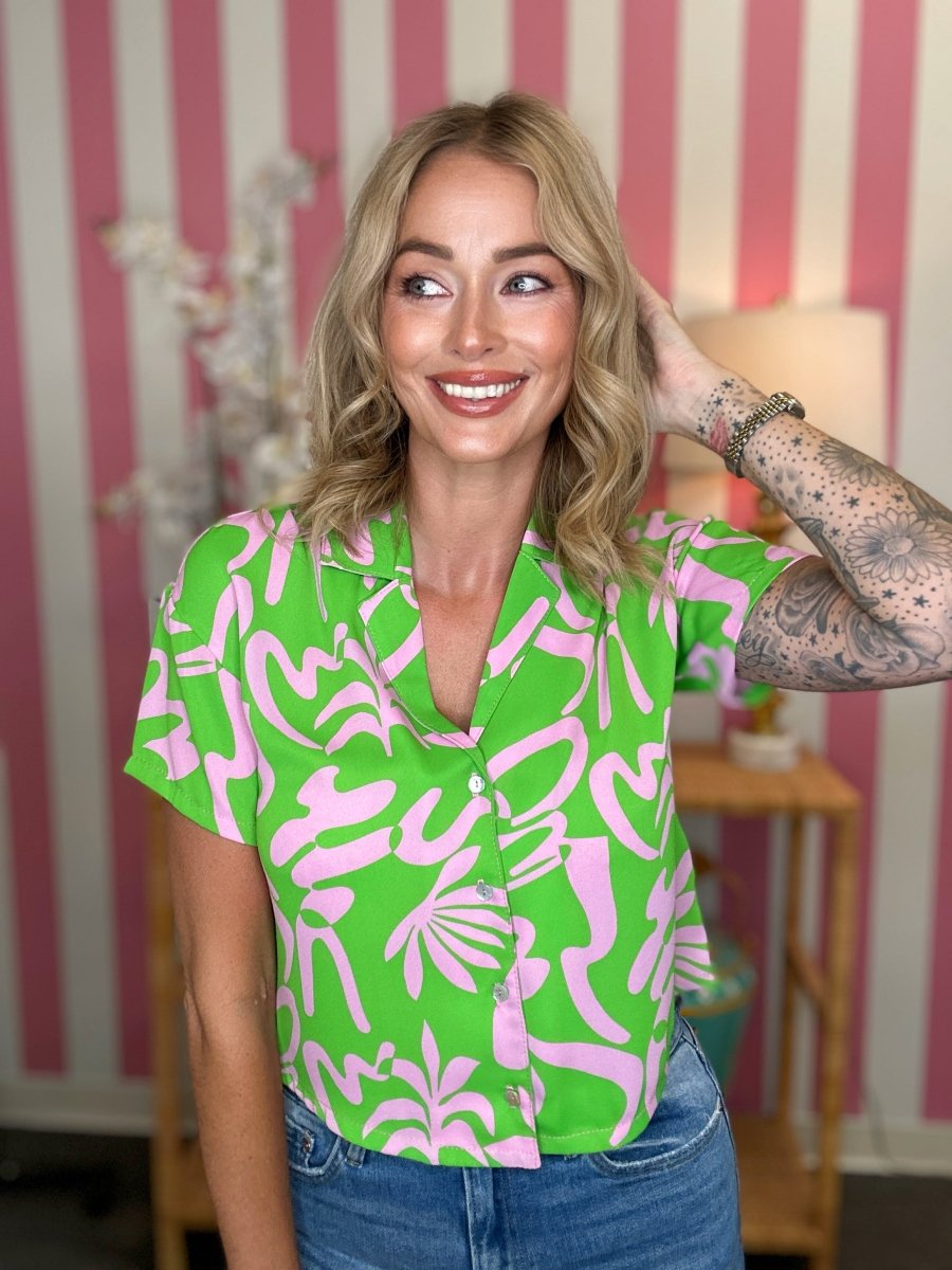 Woman wearing a green and pink patterned shirt in a room with striped wallpaper.