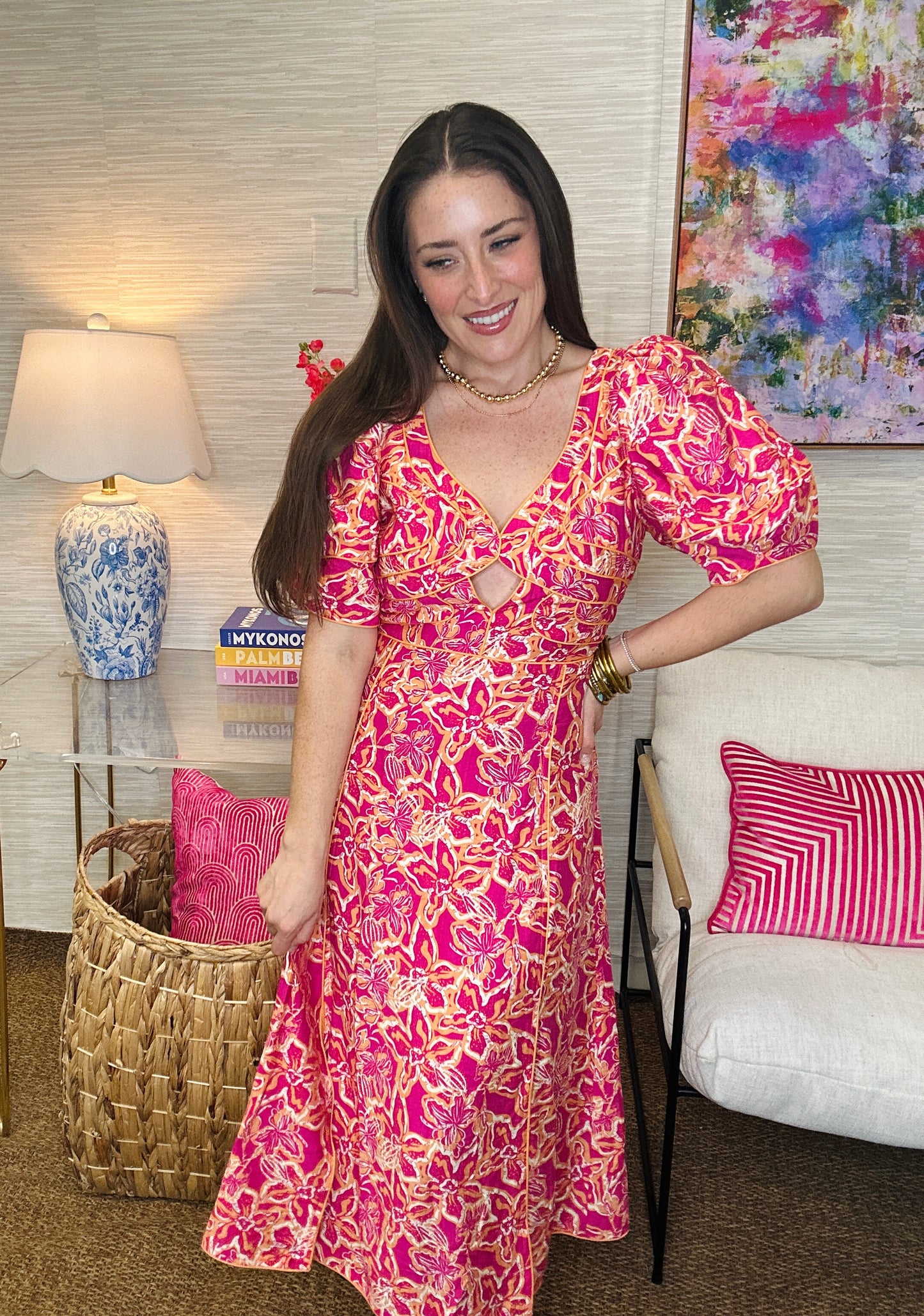 Woman in a pink floral dress standing in a living room with colorful decor.