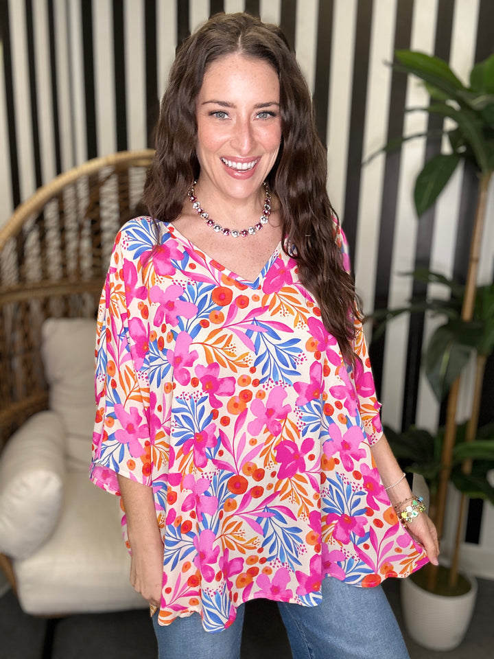 Woman wearing a colorful floral blouse in a room with a striped wall and plant.