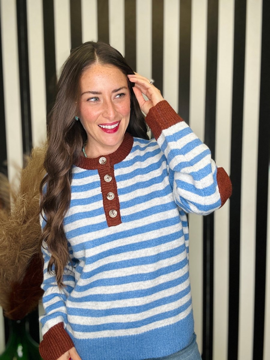 A woman wearing a blue and white striped knit sweater with brown ribbed trim and a three-button henley neckline, posing in front of a black and white striped background.