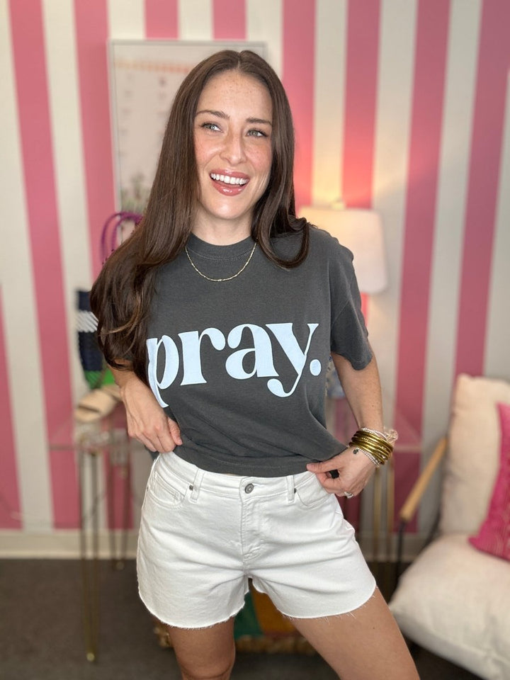 Woman wearing a black t-shirt with 'pray.' text in a casual setting.
