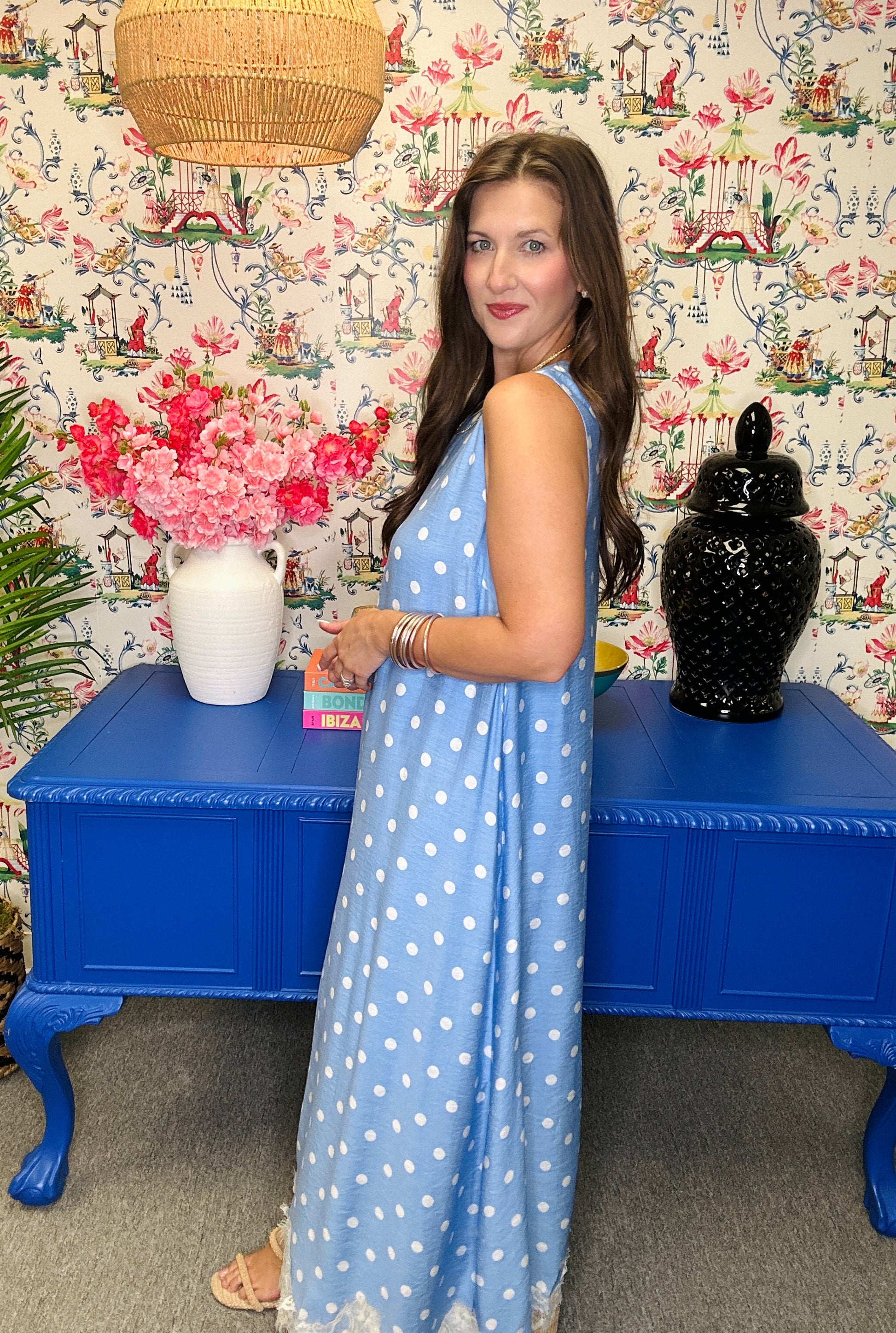 Woman in a blue polka dot dress standing in front of a colorful wall with floral patterns.