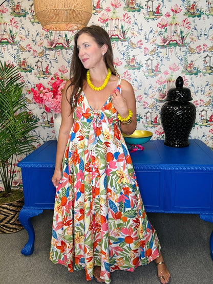 Woman in a colorful floral dress standing in front of a patterned wall with a blue table and decorative items.