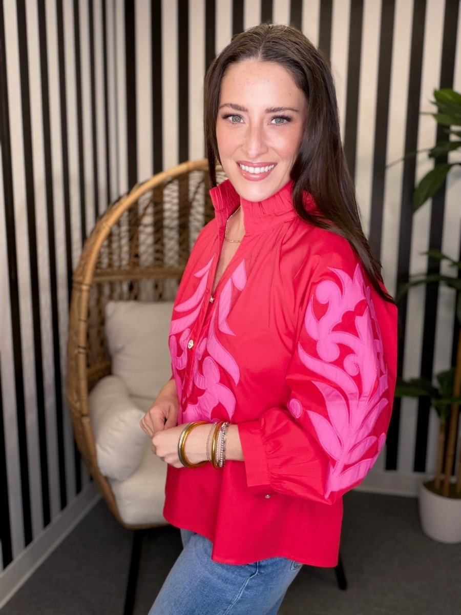 Woman wearing a red blouse with pink floral patterns in a room with striped walls and a wicker chair.