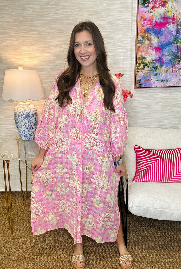 Woman in a pink floral dress standing in a room with a lamp and colorful painting.