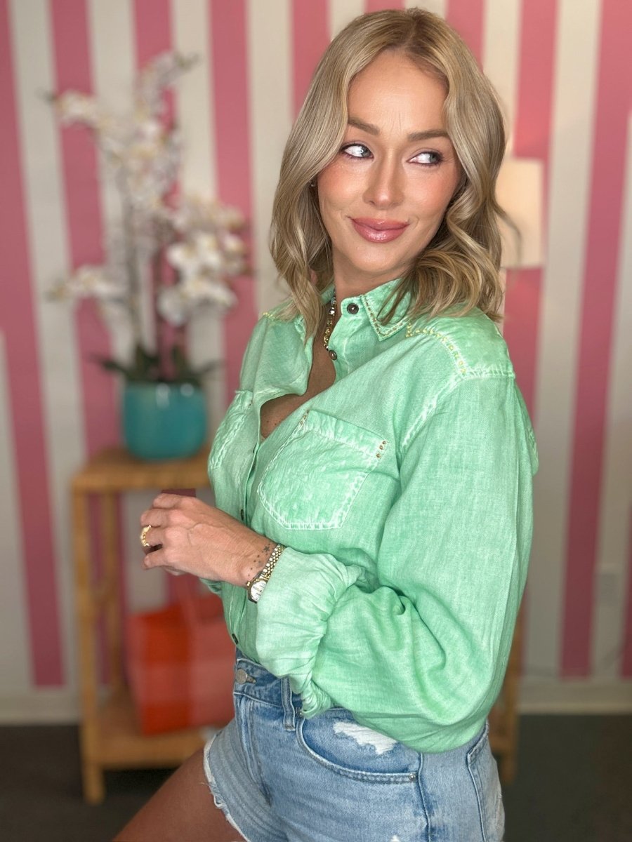 Woman wearing a green sequin top and blue jeans in a room with striped walls.