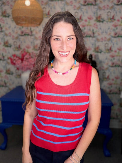 Woman wearing a red and blue striped sleeveless top in a room with floral wallpaper.