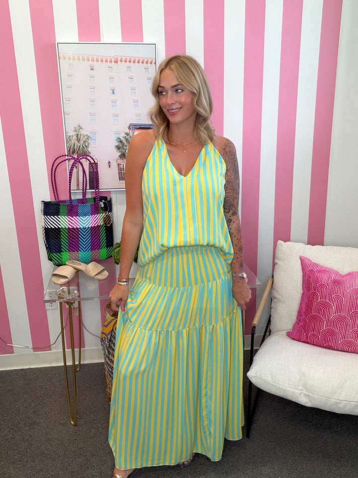 Woman in a yellow and green striped dress standing in a room with pink and white striped walls.