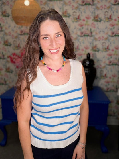 Woman wearing a white sleeveless shirt with blue stripes in a room with floral wallpaper.