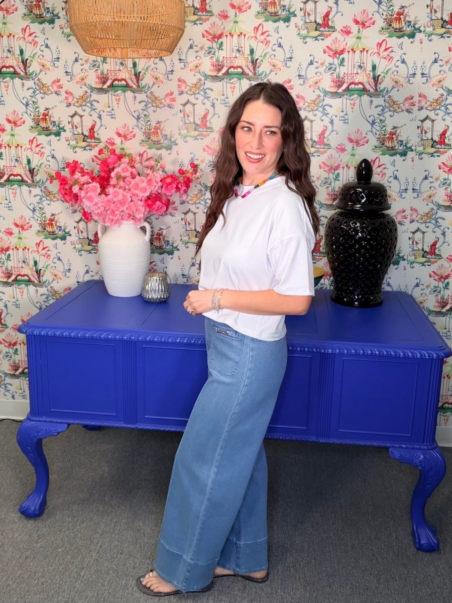 Woman standing next to a blue table with floral wallpaper in the background