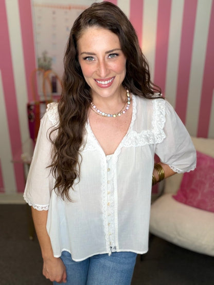 Woman wearing a white blouse with lace details in a room with striped wallpaper.