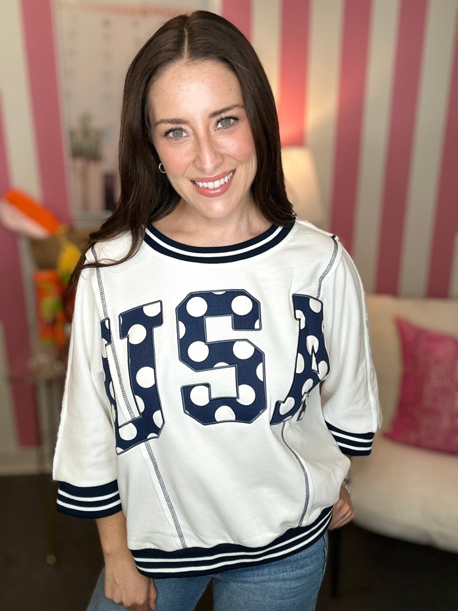 Woman wearing a white sweatshirt with 'USA' printed on it in a casual setting.
