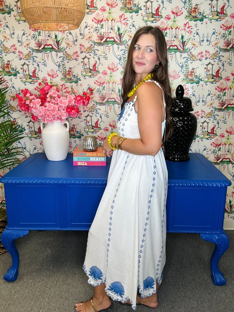 Woman in a white dress standing next to a blue table with floral decorations against a patterned wall.