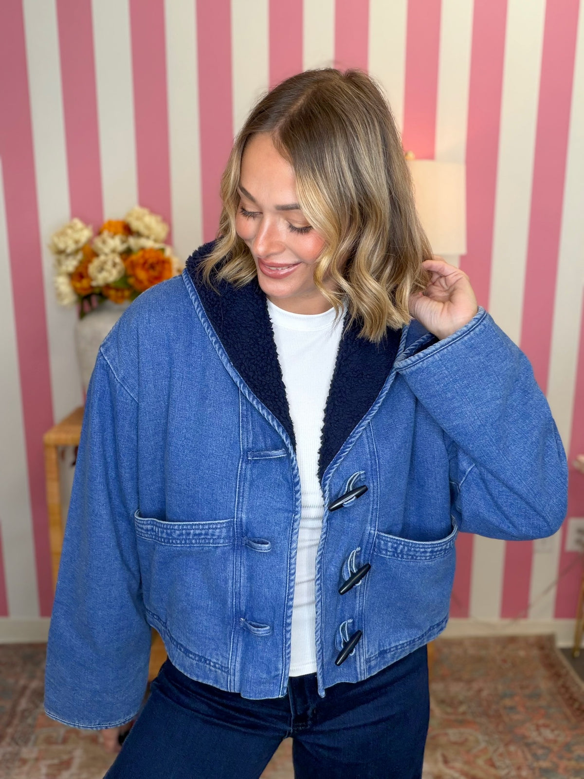 woman standing in a blue denim sherpa jacket in front of a pink striped wall