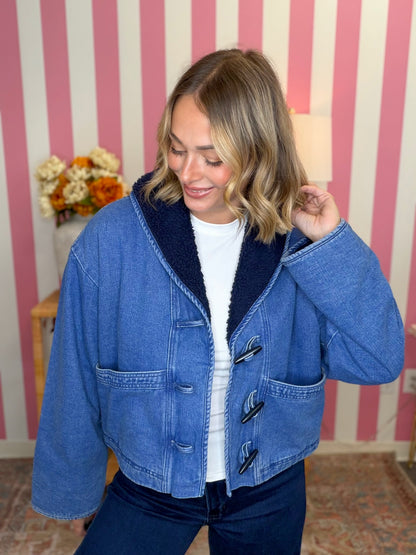 woman standing in a blue denim sherpa jacket in front of a pink striped wall