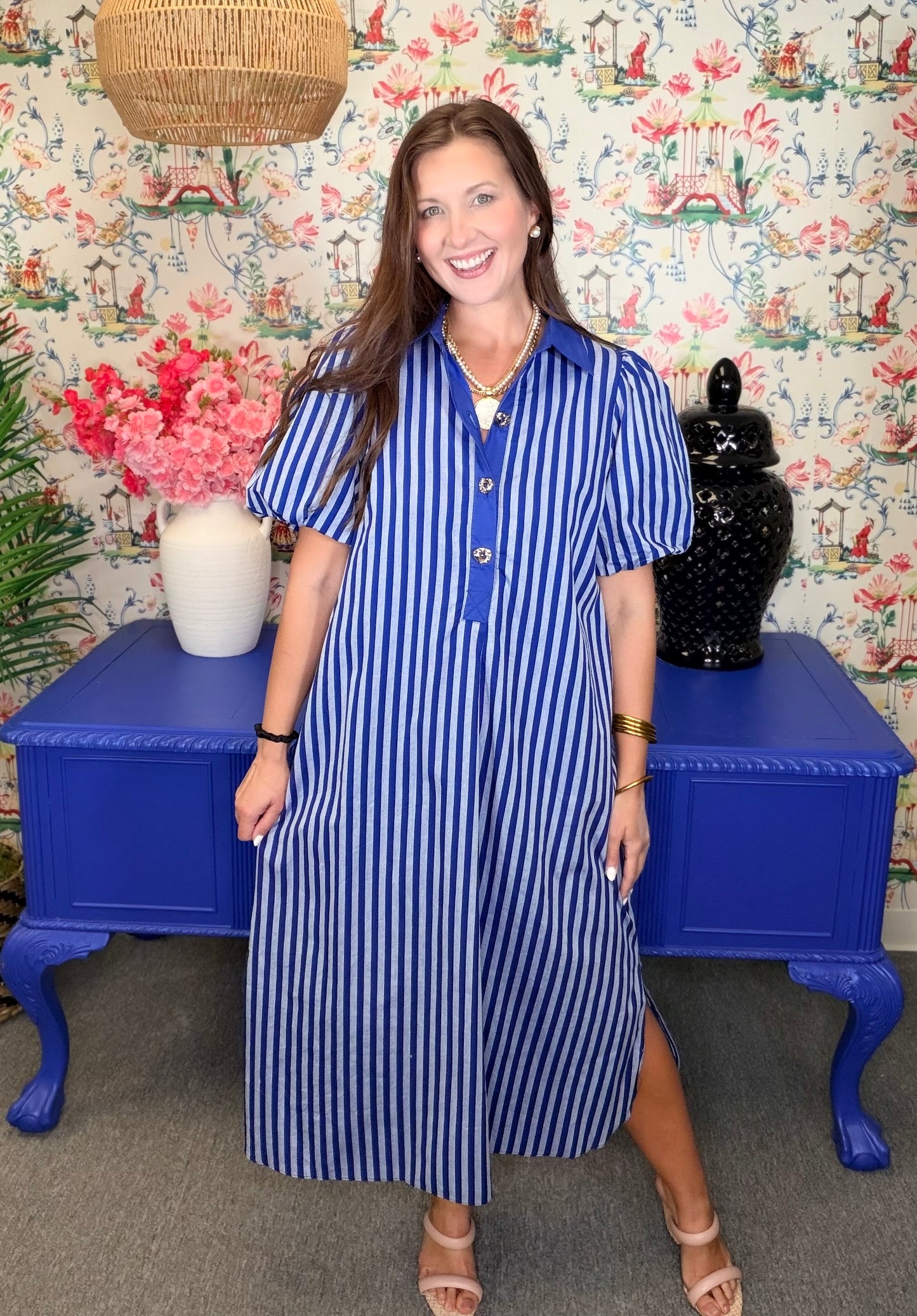 Woman wearing a blue and white striped dress standing in front of a colorful floral-patterned wall.
