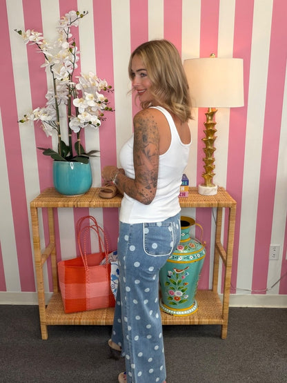 Woman standing in a room with striped walls, a lamp, and decorative items on a table.