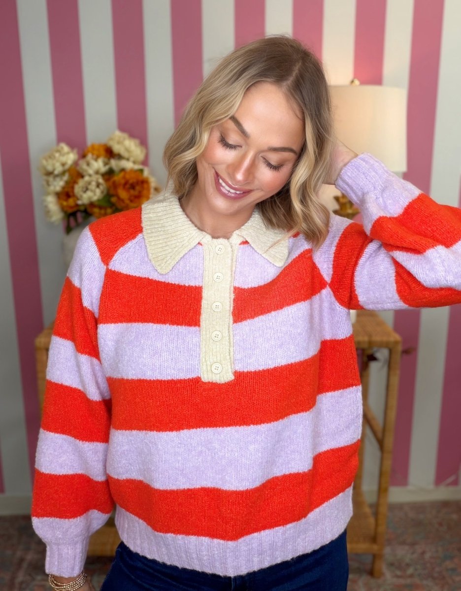 A woman wearing a fuzzy knit sweater with bold horizontal red and light lavender stripes, featuring a cream-colored knit collar and button placket. She is posing in front of a pink and white striped wall.