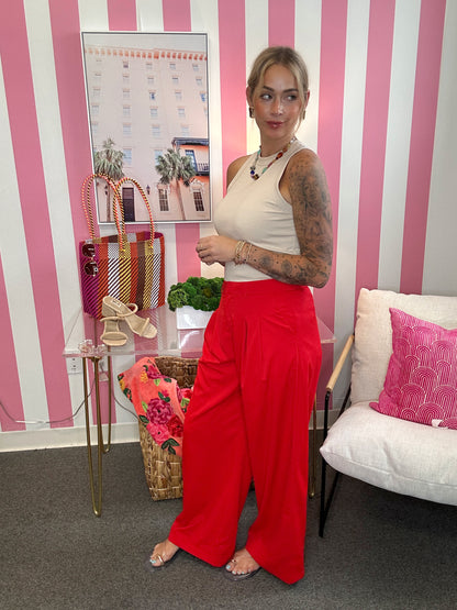 Woman in a white top and red pants standing in a room with striped walls and decorative items.