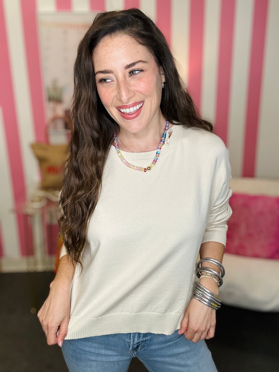 Woman wearing a white sweater and blue jeans with a striped background
