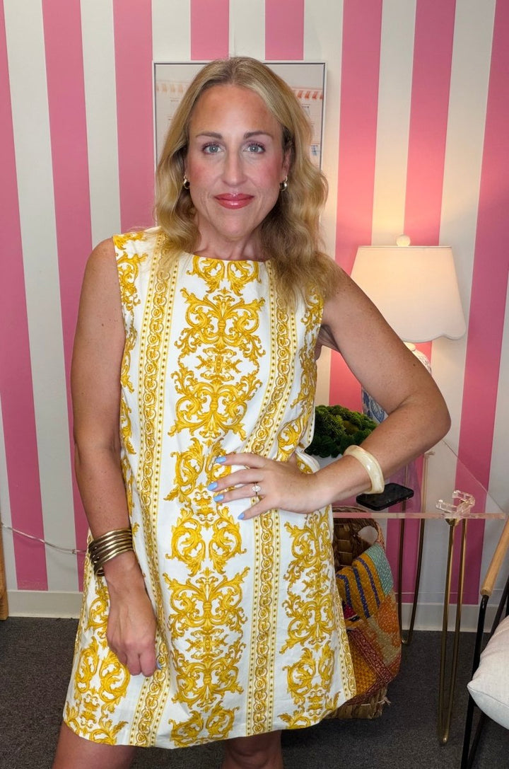 Woman wearing a yellow and white patterned dress in front of a striped wall.