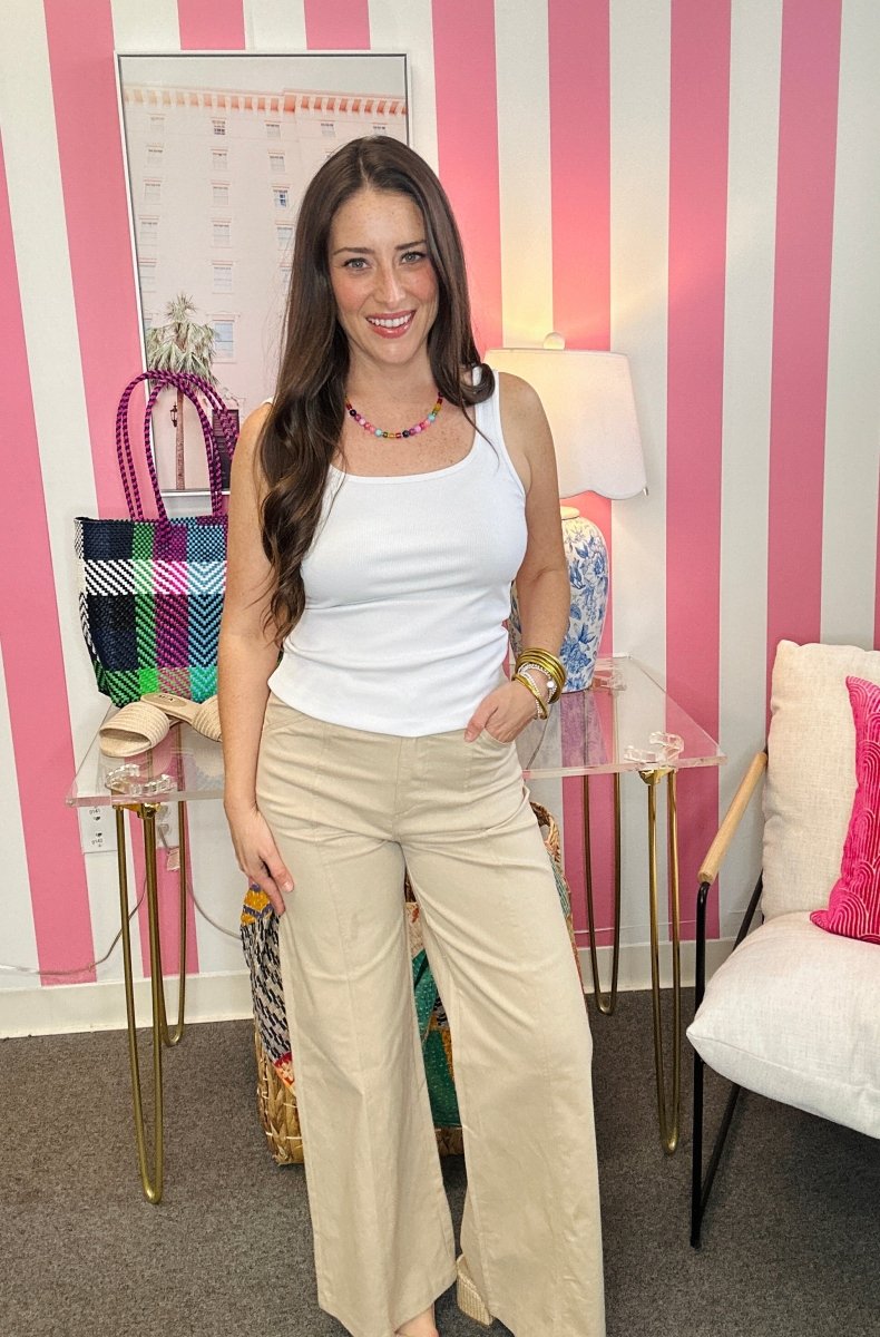 Woman in a white top and beige pants standing in a room with striped walls and furniture.