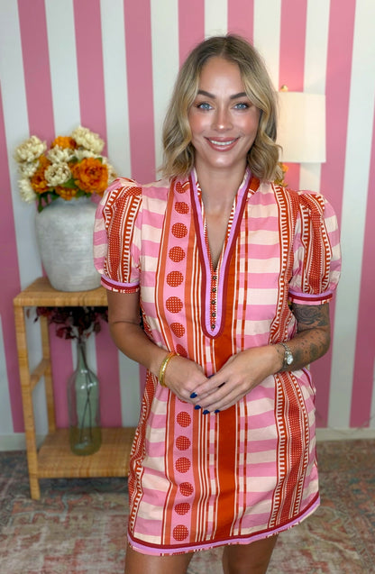 woman standing in a colorful multi patterned short sleeve dress with a v-neck