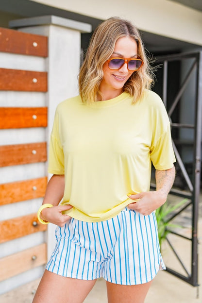 Woman wearing a yellow top and blue striped shorts standing in front of a colorful wall.