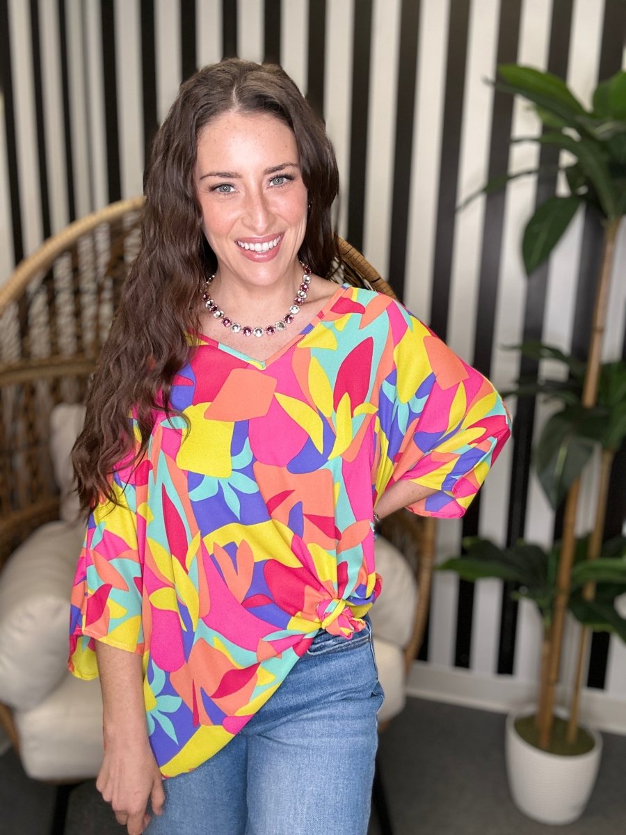 Woman wearing a colorful patterned top in a room with striped walls and a plant.