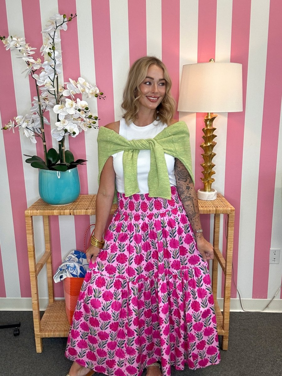 Woman in a pink floral dress with a green shawl standing in front of a striped wall.