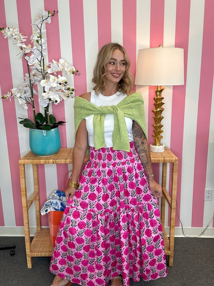 Woman in a pink floral dress with a green shawl standing in front of a striped wall.